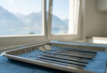 Eine Nahaufnahme von sterilen zahnärztlichen Instrumenten auf einem Tablett in einer modernen Praxis. Im unscharfen Hintergrund ist durch ein Fenster eine ruhige Landschaft der Schweizer Alpen zu sehen.