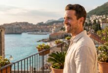 Ein glücklicher Mann mittleren Alters mit einem perfekten weißen Lächeln auf einem Hotelbalkon, im unscharfen Hintergrund die sonnige Küste der Türkei.