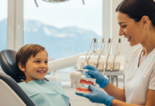 Ein lächelndes Kind im Zahnarztstuhl mit einem freundlichen Kinderzahnarzt, der eine Zahnbürste und ein Zahnmodell zeigt, in einer modernen und hellen Schweizer Praxis. Im stark verschwommenen Hintergrund sind die weichen Umrisse von Bergen zu erkennen.
