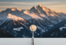 A close-up, sharp-focus shot of a modern, sterile dental mirror resting on a clean surface. In the soft, out-of-focus background, the majestic, snow-capped peaks of the Swiss Alps are visible under warm, cinematic lighting.