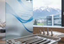 Close-up of sterile, high-tech dental instruments on a clean tray inside a modern clinic, with a blurred view of the Swiss Alps visible through a window in the background. The scene suggests meticulous care and advanced dental procedures.