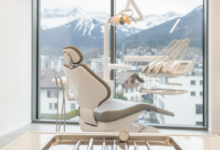 A clean, modern dental clinic room with advanced instruments on a tray in the foreground and a comfortable dental chair in the mid-ground. Through a large window, a blurred view of a Swiss city and mountains is visible in the background, conveying high-quality dental care in Switzerland.