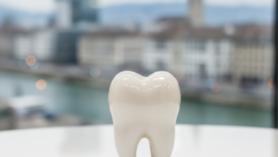 A detailed, close-up photograph of a pristine white ceramic dental crown on a clean, bright surface. The background is softly blurred, revealing architectural elements of the Basel city skyline.